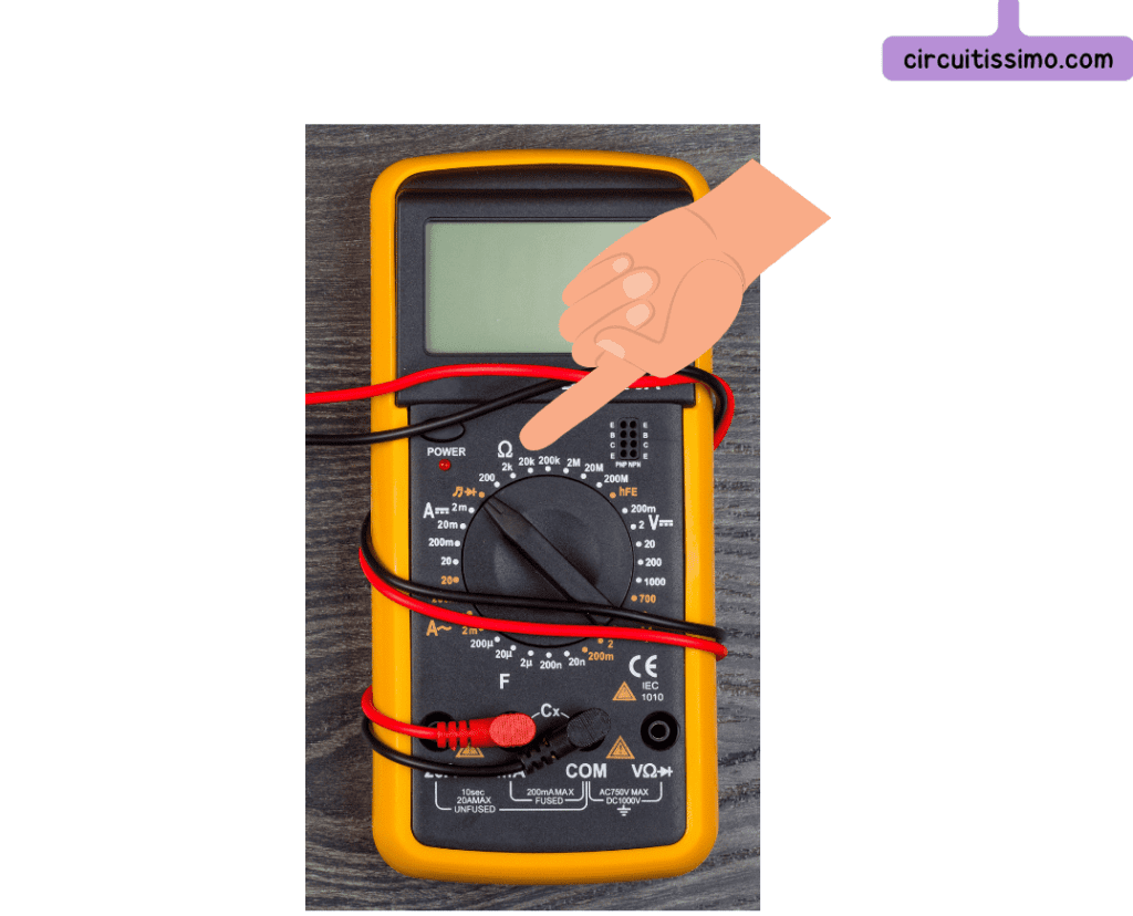 Multimètre numérique avec des cordons de test connectés, affichant un cadran pour mesurer la résistance. Un doigt pointe sur le réglage d'ohm.